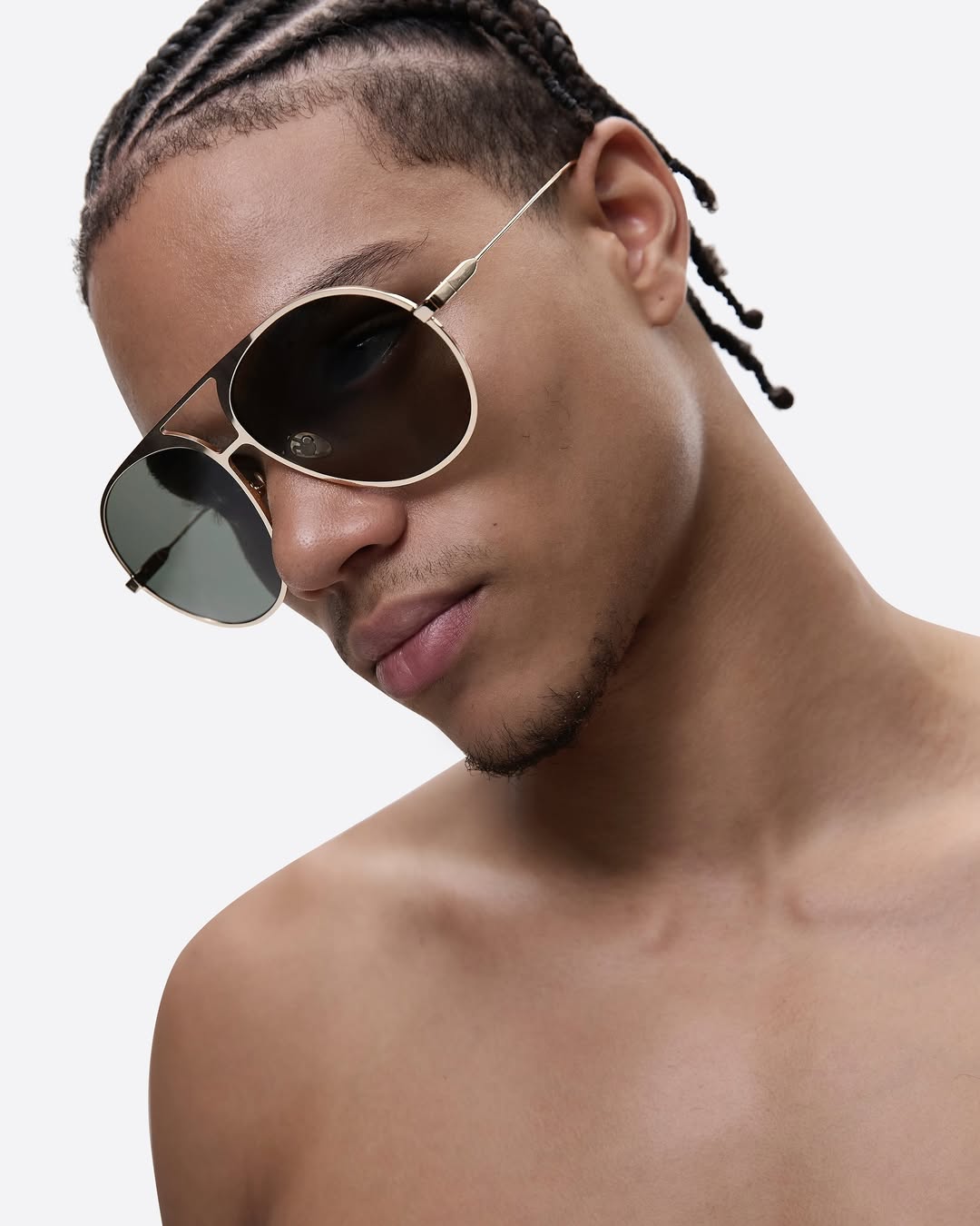 Close-up of a shirtless adult male wearing gold aviator sunglasses with a white background, highlighting fashion and style.