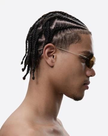 Profile view of adult male with dark braided hair and sunglasses, on a light background in a studio setting. Minimalist fashion shot.