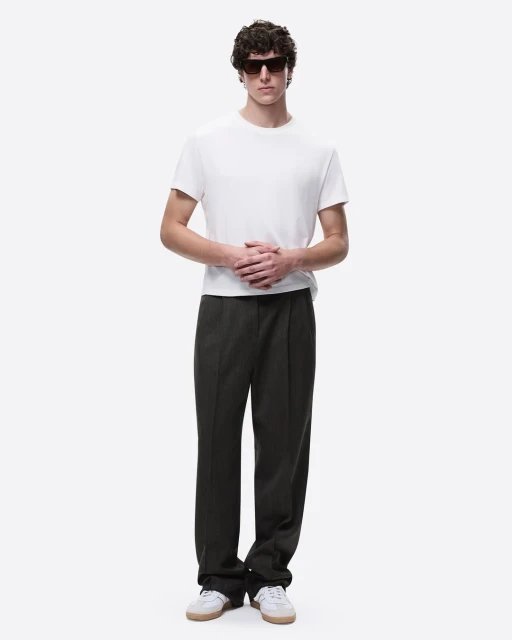 Full-length shot of a young adult male model wearing a white t-shirt, dark pants, sunglasses, and sneakers against a white background.