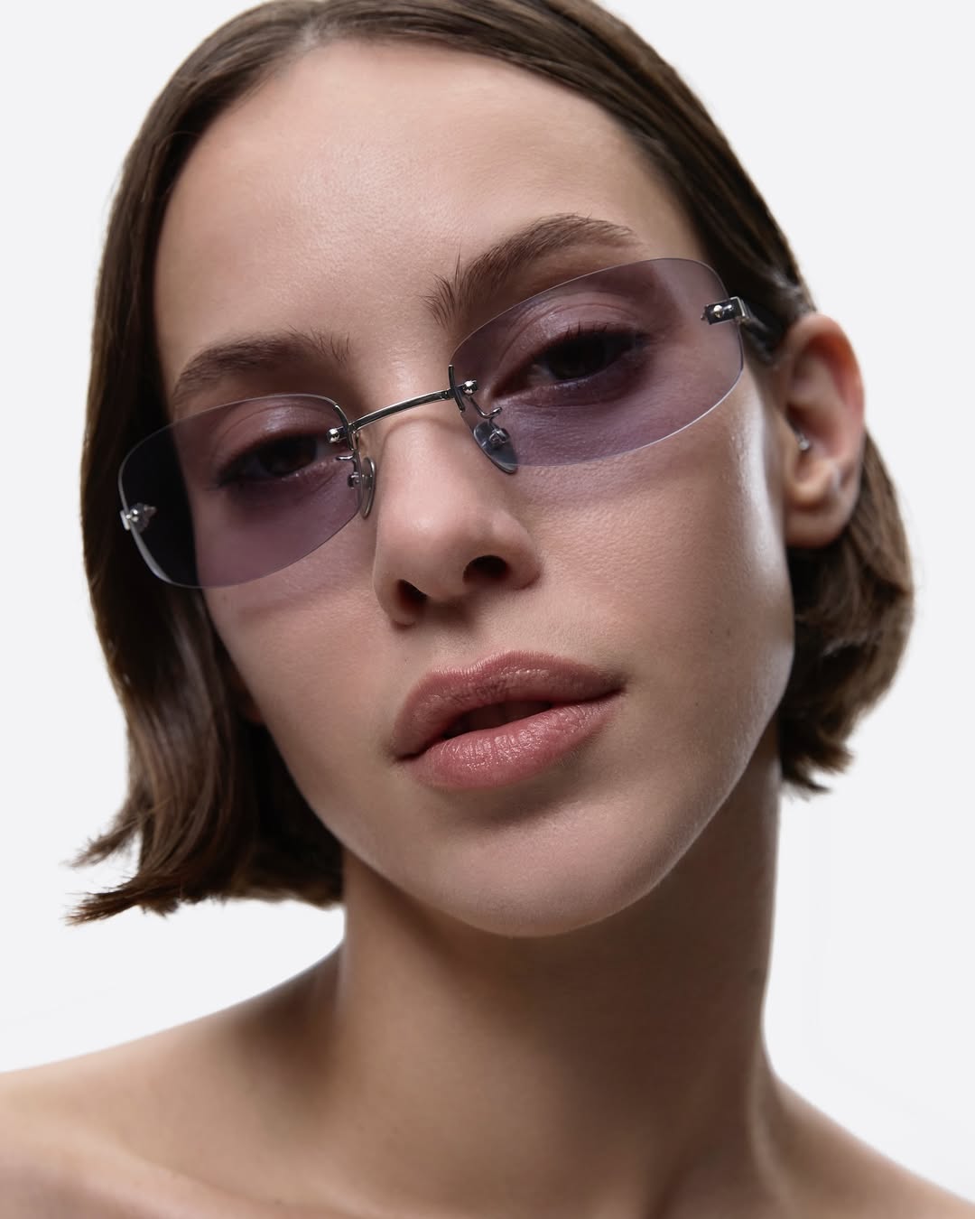 Close-up of an adult woman wearing rimless sunglasses with tinted lenses against a white background in a studio shot.