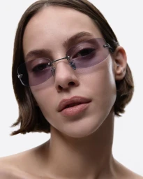 Close-up portrait of a woman wearing tinted frameless sunglasses against a plain white background