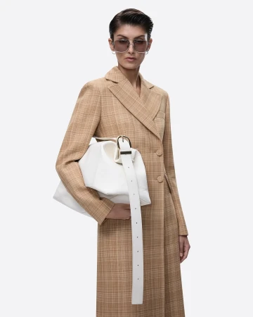 Model wearing tinted sunglasses and a tan patterned coat holding a white structured handbag against a plain background