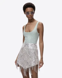 Model wearing tinted sunglasses, a light green scoop-neck tank top, and a sparkling silver fringed miniskirt against a plain white background.