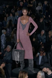 Model in a mauve dress and thigh-high boots holding a grey handbag on a runway for Diesel Resort 26