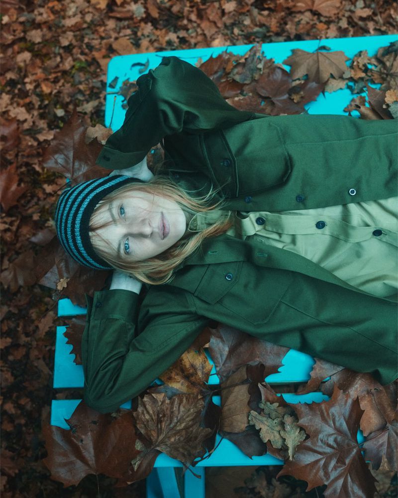 Overhead shot of a fair-skinned person lying on a light blue bench amidst fallen brown leaves in an outdoor autumn setting.