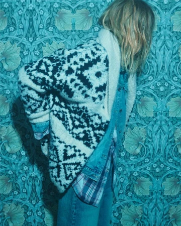 Model Julia Nobis wearing a chunky patterned cardigan and denim shirt against turquoise wallpaper