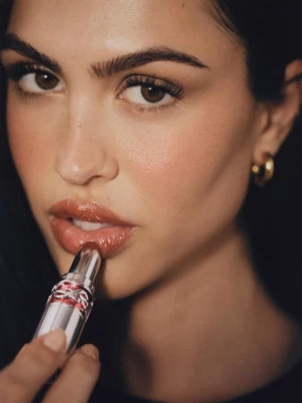 Close-up of a woman applying lip gloss, showcasing beauty and makeup with a focus on the cosmetic product and the model's features.