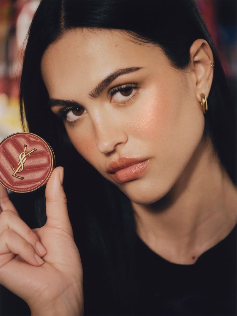 Close-up of a brunette woman holding Yves Saint Laurent blush with a gold logo, showcasing makeup and cosmetics, shot indoors.