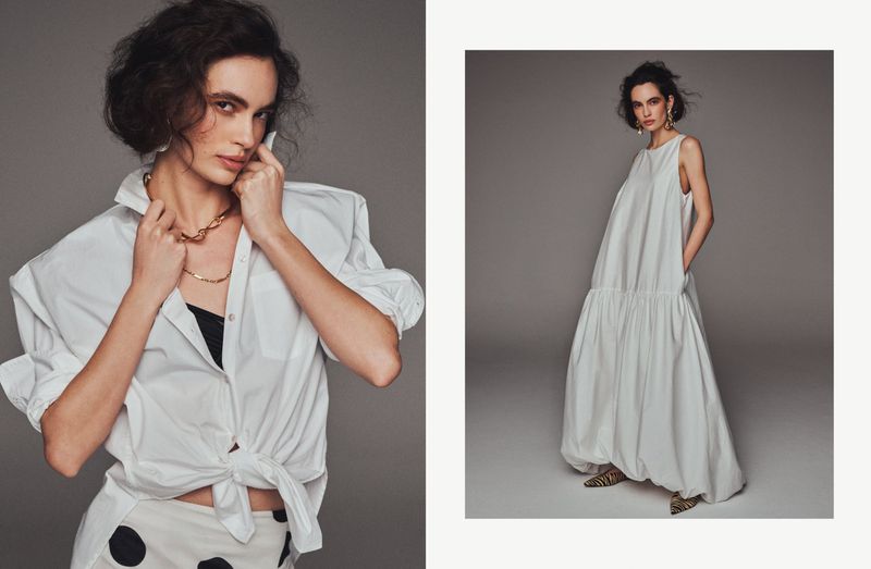 Fashion shot of a woman in a studio wearing a white shirt tied at the waist and a spotted skirt, and another wearing a white dress.