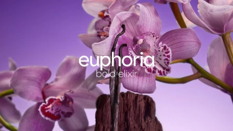 Close-up commercial shot of purple orchid flowers and dark vanilla bean pods against a soft purple background for Calvin Klein.