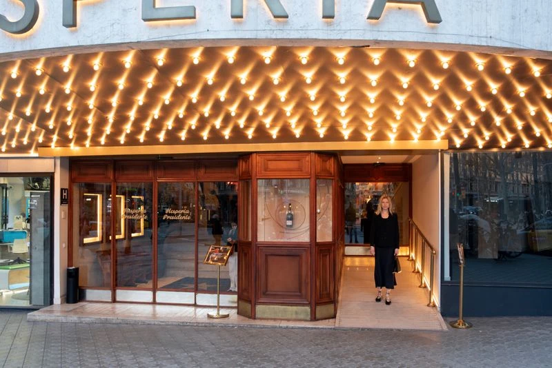 Woman exits a commercial building with a brightly lit awning. The architecture has wood and glass features, with street view in the back.