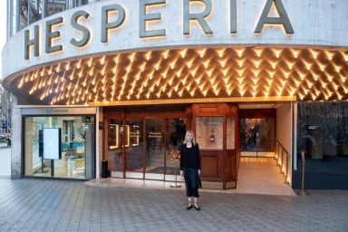 Woman standing in front of hotel entrance with lit canopy sign for Asket advs