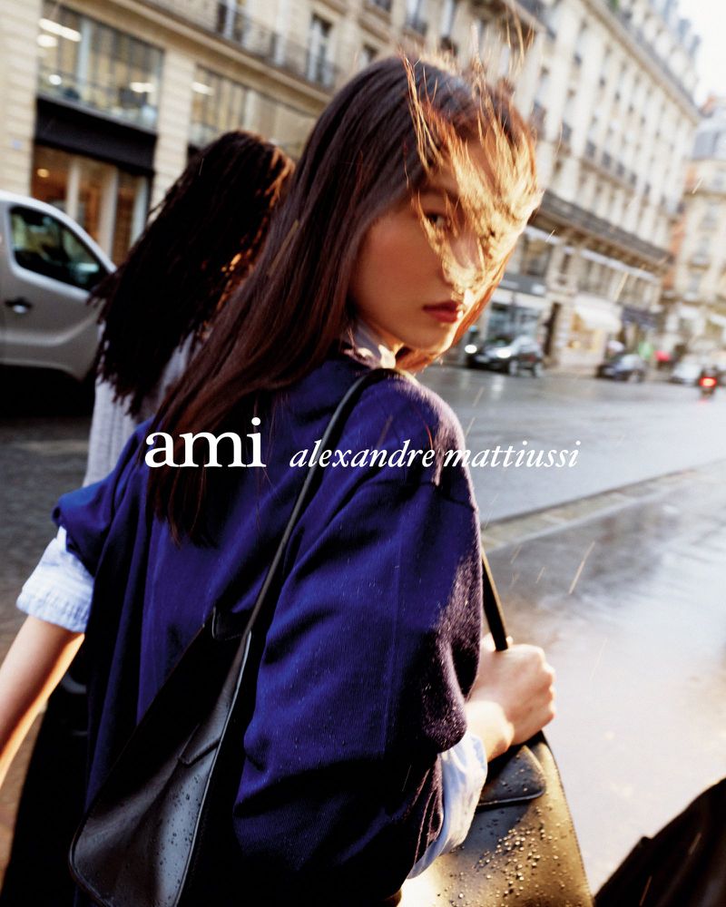 Fashion shot features a young Asian woman with long hair, blue top, black bag, looking back over her shoulder on a city street.
