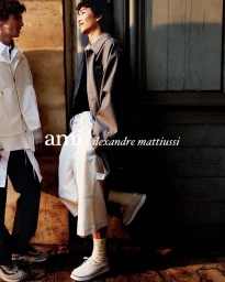 Two young men in casual attire leaning against an urban wall for the Ami spring summer 2026 campaign.