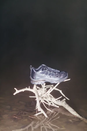 A dark sneaker resting on a bleached branch structure set against a dark, moody background for the OAMC x Salomon collaboration.