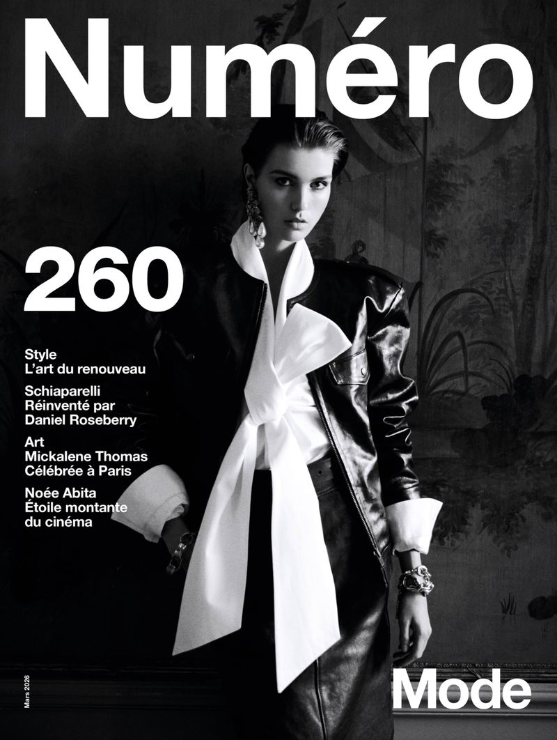 Black and white fashion magazine cover featuring a model in a stylish jacket and oversized bow, complemented by bold typography and artistic backdrop.