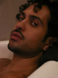 Close-up portrait of Mahmood reclining in a white bathtub with dark curly hair and a mustache for Butt Magazine photographed by Luke Abby