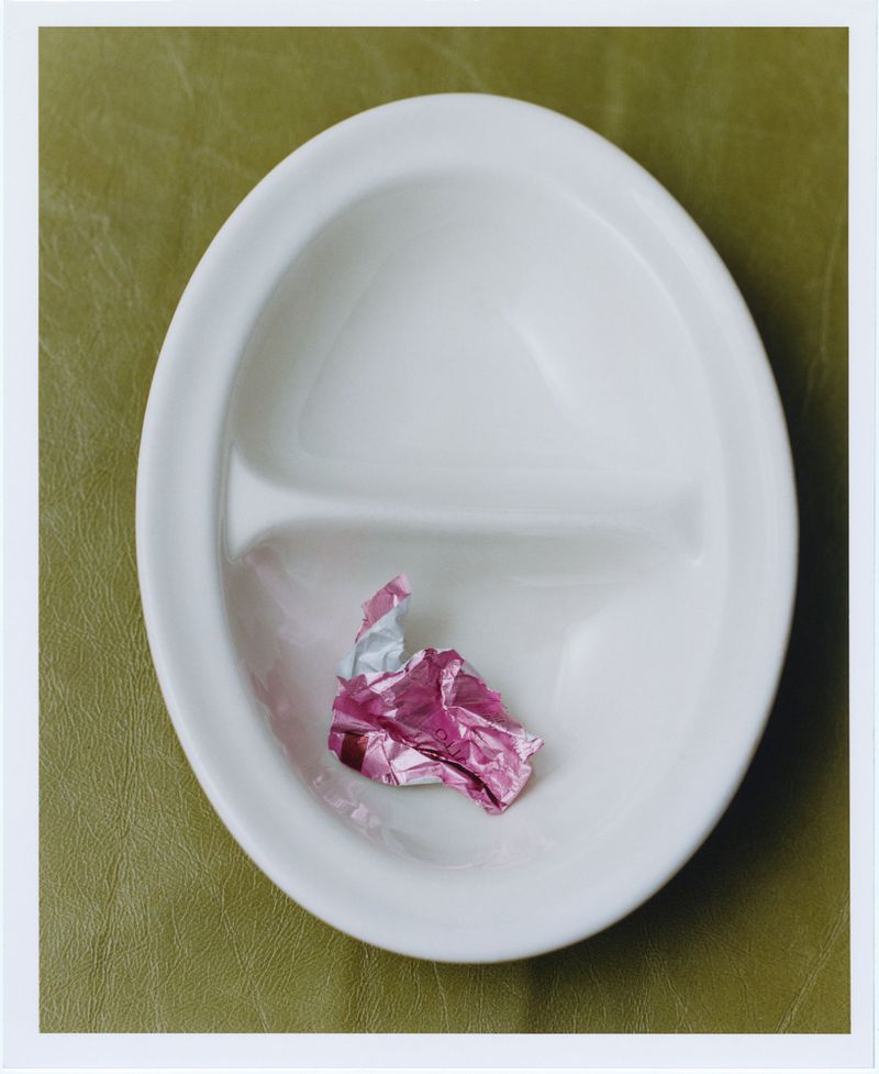 Close-up of a white divided serving dish on a green surface, containing a crumpled piece of shiny pink wrapping foil.