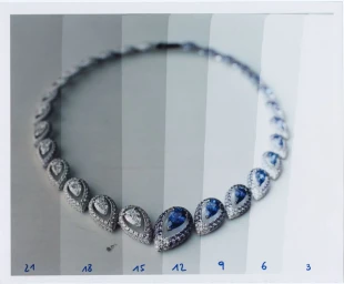 Close-up of a diamond and sapphire teardrop necklace displayed across vertical gray tone gradient strips.