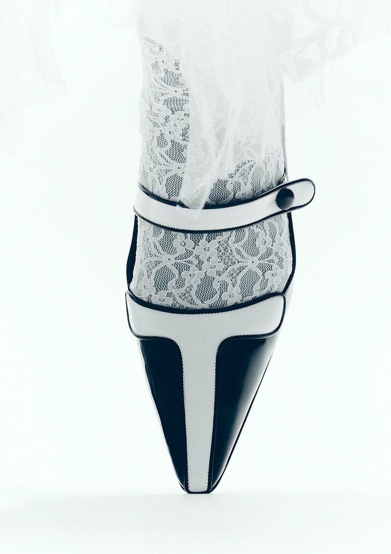 Black and white high heel shoe with lace ankle detail on white backdrop, studio lighting.