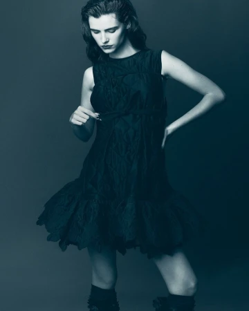 Model in a dark sleeveless dress posing against a solid grey background for Elle Hungary