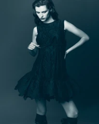 Model in a dark sleeveless dress posing against a solid grey background for Elle Hungary