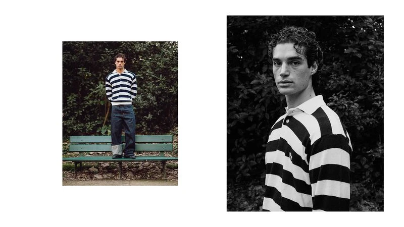 A young man stands on a bench in a striped shirt and jeans in an outdoor fashion editorial, captured in a bright, natural light.