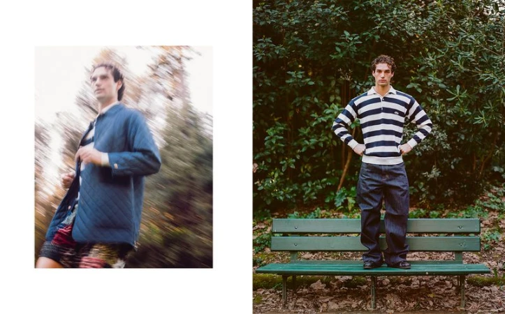 A male fashion model poses on a park bench in a striped sweater, while another blurry male figure walks amidst foliage in a blue coat.