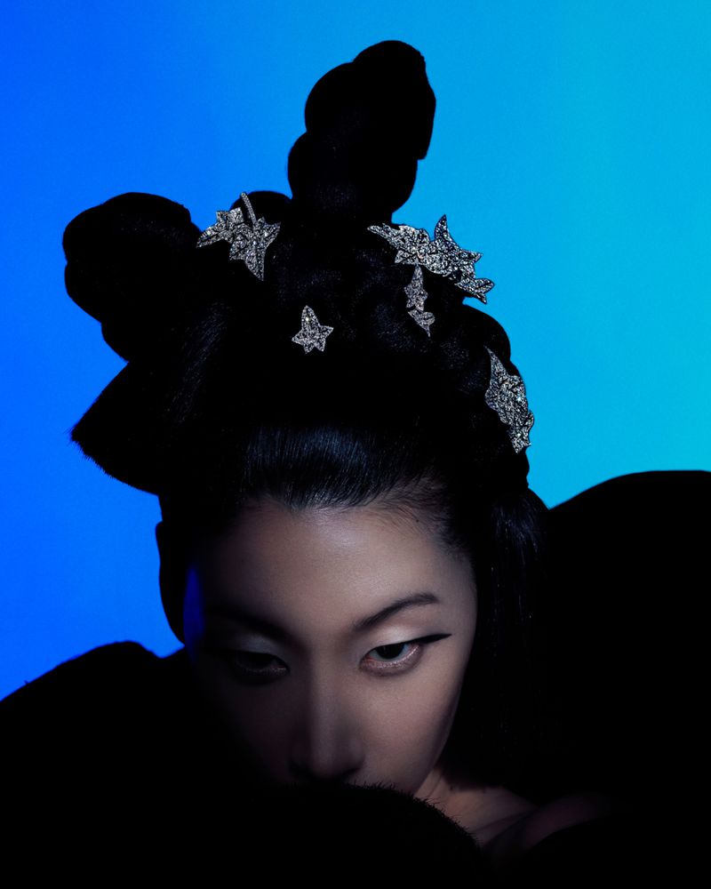 Asian woman with stylish black updo and star hair clips posing in a beauty portrait against a blue gradient background in studio lighting.