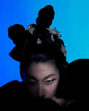 Asian woman with stylish black updo and star hair clips posing in a beauty portrait against a blue gradient background in studio lighting.