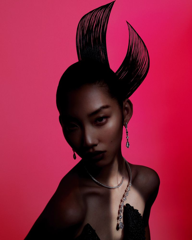 Stunning portrait of an adult female with unique hairstyle and ornate jewelry on a bright pink background, fashion editorial look.