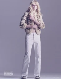 Model with long blonde hair wearing a cream shearling jacket and white trousers against a neutral background for Dazed Magazine.
