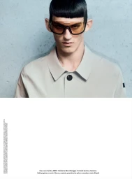 Portrait of a male model wearing tinted wraparound sunglasses and a light grey collared shirt against a mottled blue-grey background.