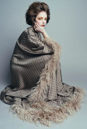 Woman in patterned coat with feather trim posing in a studio with soft, diffused lighting and neutral background for a fashion editorial.