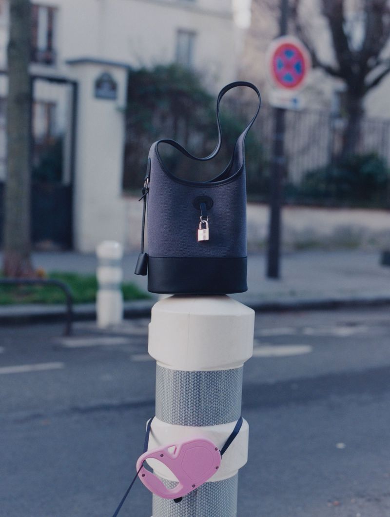 Elevated view of a black leather handbag with a padlock on top of a white bollard with a pink dog leash attached in an urban setting.