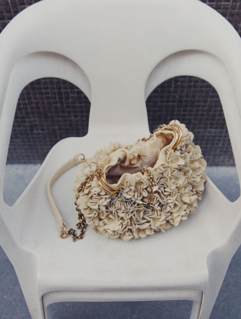 Floral textured purse in cream and gold on a white chair, in a softly lit indoor setting, fashion accessory, purse, floral, gold accents.