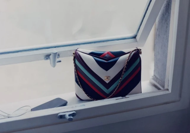 Multicolor chevron-striped leather handbag resting on a white window sill next to a smartphone