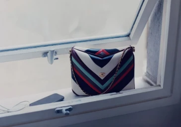 Multicolor chevron-striped leather handbag resting on a white window sill next to a smartphone