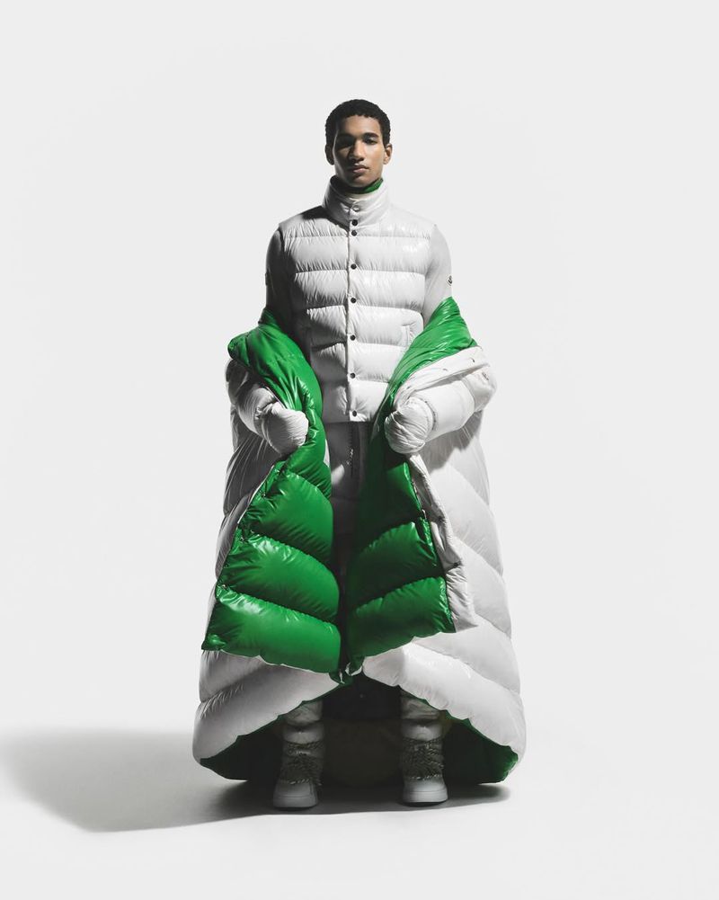 A man wearing an oversized white puffer coat with green lining over a white quilted jacket against a seamless white background.