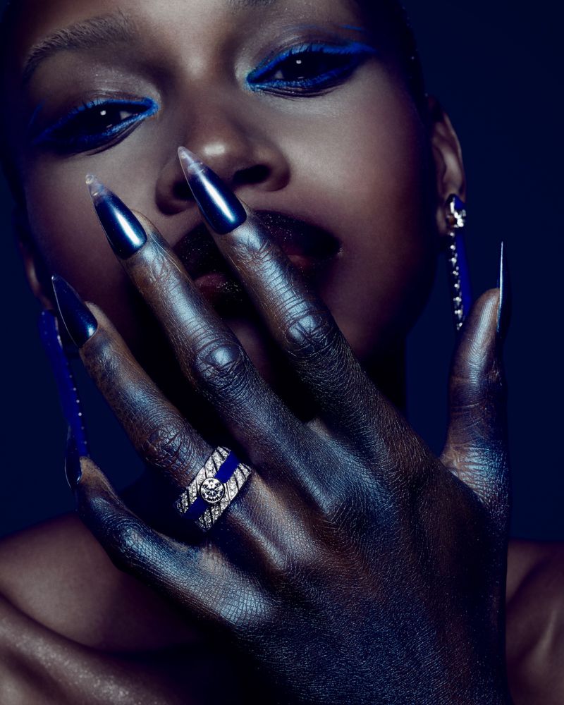 Close-up fashion shot of a Black female model with dramatic blue eye makeup, glossy dark lipstick, and long, dark, glossy fingernails.