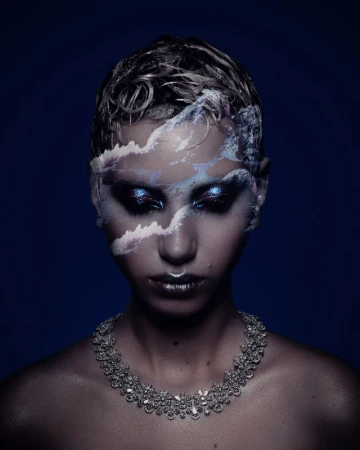Portrait of a woman with silver wet-look hair and elaborate jewel necklace, a cloudy mountain landscape reflected on her face.
