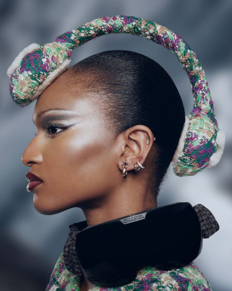 Close-up of an African-American female model wearing colorful tweed earmuffs and sunglasses, accessorized with silver eyeshadow and jewelry.