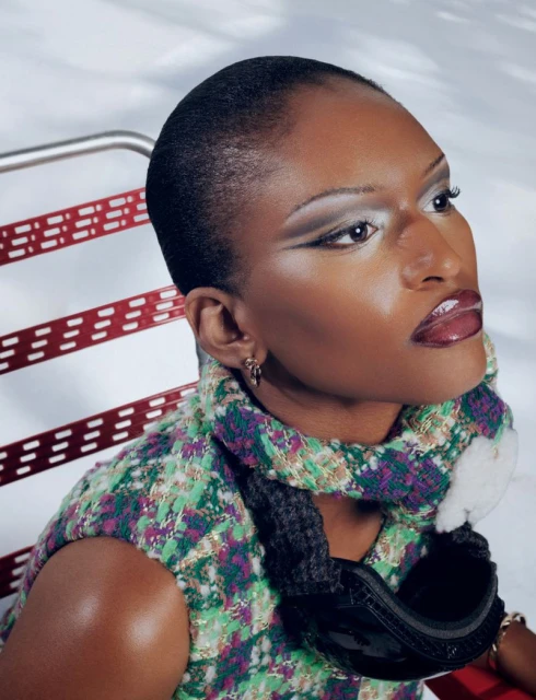 Close-up studio shot of an adult female model with neutral expression and bold makeup, wearing a green and purple patterned top.