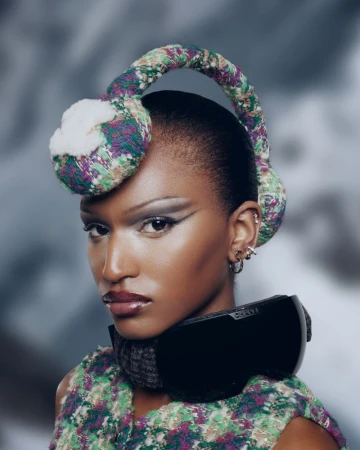 Portrait of a Black woman with stylish earmuffs and ski goggles, dramatic eye makeup, and glossy lips against a blurred winter backdrop.