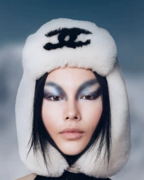 Close-up portrait of a model wearing a white furry ushanka hat with a black logo and dramatic blue eye makeup.