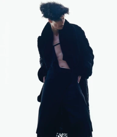 Model wearing a black coat and textured hat against a bright white background for The Face Magazine