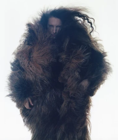 Model wearing a voluminous dark fur coat with long wild hair against a bright white background for The Face Magazine.