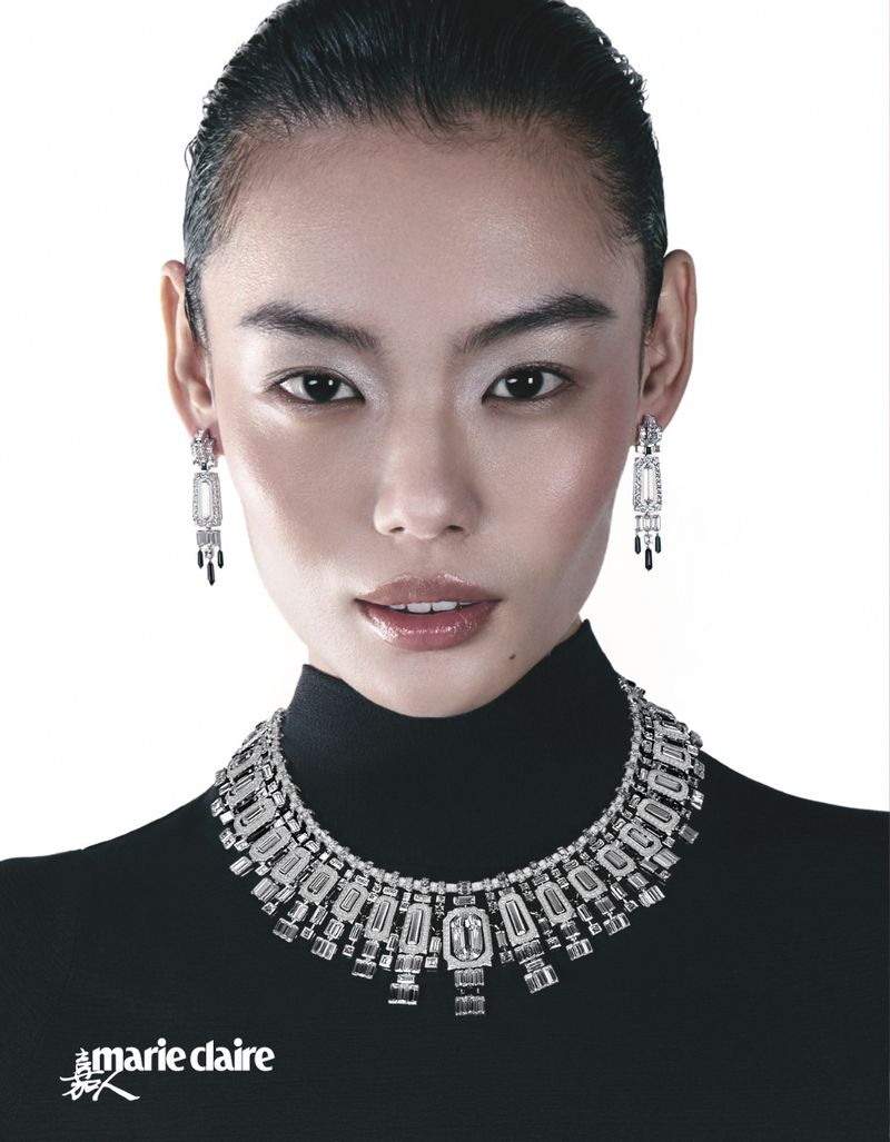 Headshot of an Asian woman with an elegant white and black diamond necklace and earrings, wearing a black turtleneck, against white.