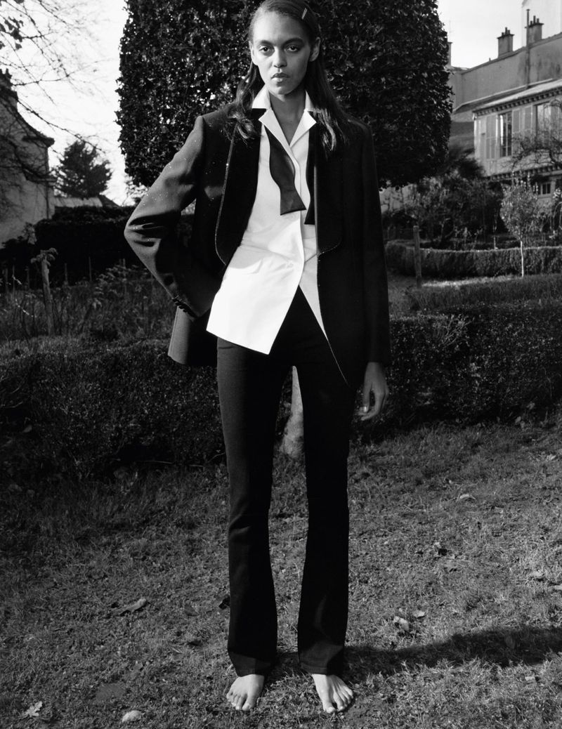 Model standing barefoot in a garden wearing a black blazer, white shirt, and bow tie for Self Service by photographer Stef Mitchell.