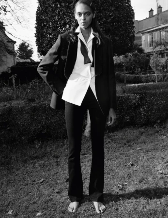 Model standing barefoot in a garden wearing a black blazer, white shirt, and bow tie for Self Service by photographer Stef Mitchell.